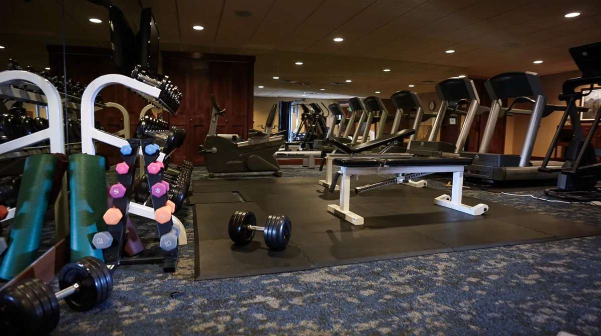 This image showcases a well-equipped fitness room featuring dumbbells, treadmills, a weight bench, and exercise mats. The space is bright and inviting, suitable for both group and solo workout sessions. The arrangement and atmosphere suggest easy access to active amenities, supporting an energetic lifestyle.