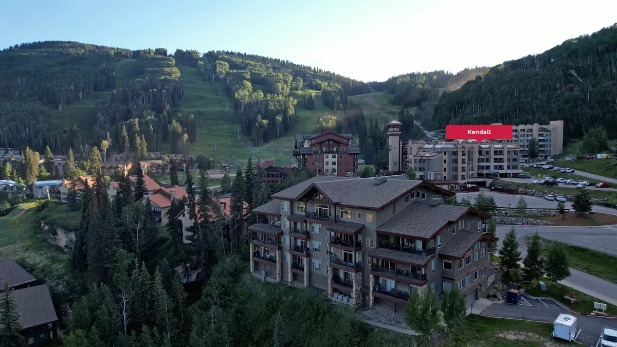 A tranquil exterior view featuring resort buildings nestled among trees, with mountains in the background. The scene encapsulates the vibrant community atmosphere of the village, suggesting easy access to shops, restaurants, and recreational activities.
